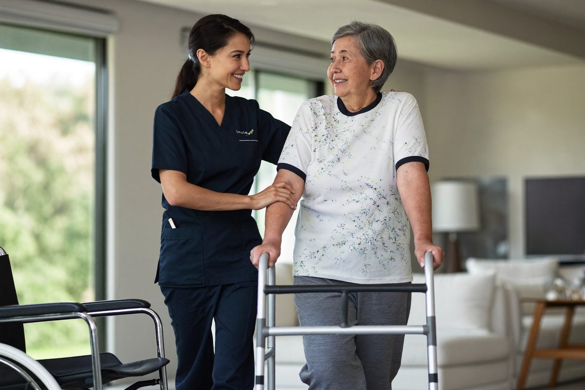 A care worker helping an older woman walk with a frame
